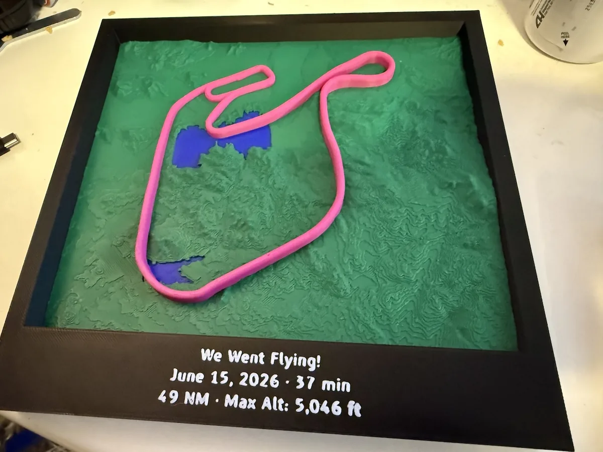 A finished print: a green relief map of southern California terrain in a black frame, with a pink flight path standing above it and the flight's date, duration, distance and maximum altitude on the frame below
